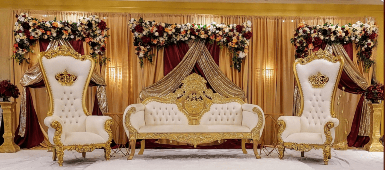 A white couch with gold trim and flowers on the wall.